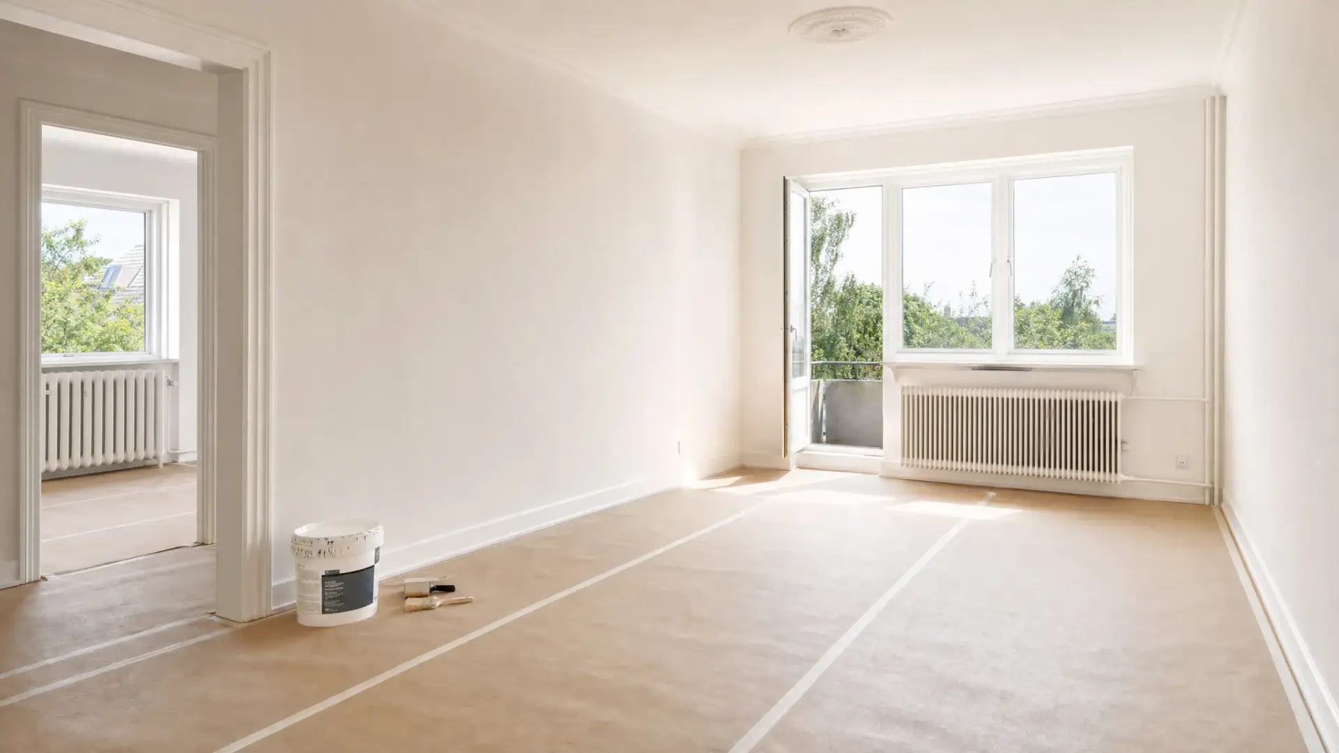 En lys stue i en bolig i Lyngby med nymalede vægge, afdækket gulv, malerspand og rene pensler placeret ved fodlisten. Rummet fremstår enkelt, ryddeligt og klar til indflytning.