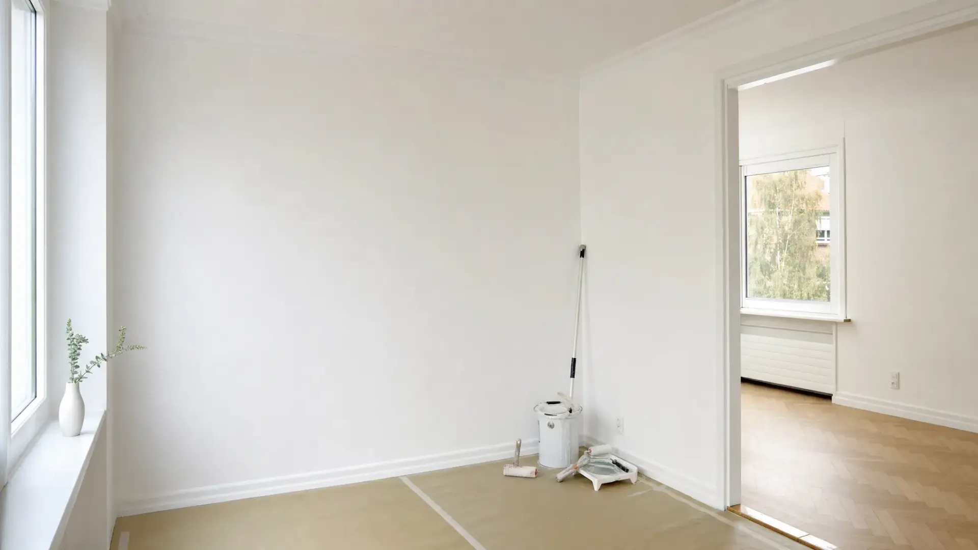 Lys lejlighed set i nærmere udsnit med nymalede vægge og loft, afdækket gulv langs panelerne og malergrej samlet diskret ved væggen, så resultatet fremstår rent og ensartet.