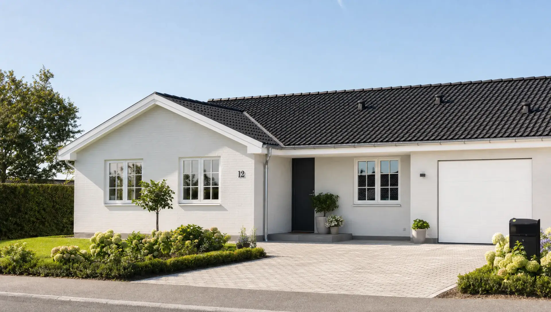 Et nymalet dansk parcelhus set udefra i øjenhøjde med lyse facader, velholdt træværk og store vinduer, hvor huset fremstår roligt, moderne og ensartet i dagslys.