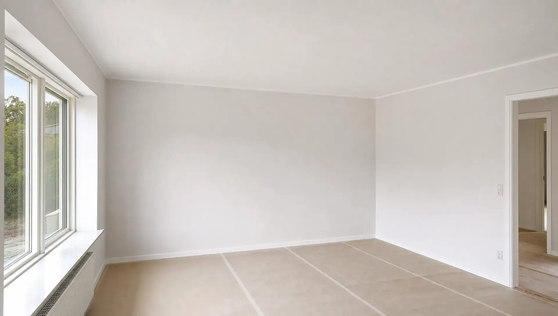 Nymalede lyse vægge og lofter i en tom stue i et dansk hjem, set i øjenhøjde mod hjørnet af rummet, med afdækket gulv og rene overgange ved loft og vægge, der viser professionelt indvendigt malerarbejde.
