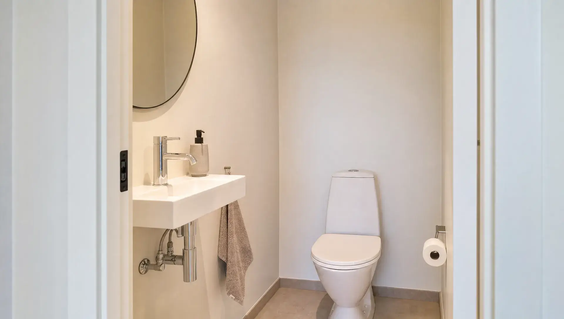 Et nymalet gæstetoilet med rene vægge, en håndvask, pæne karme og et lyst, enkelt udtryk.
